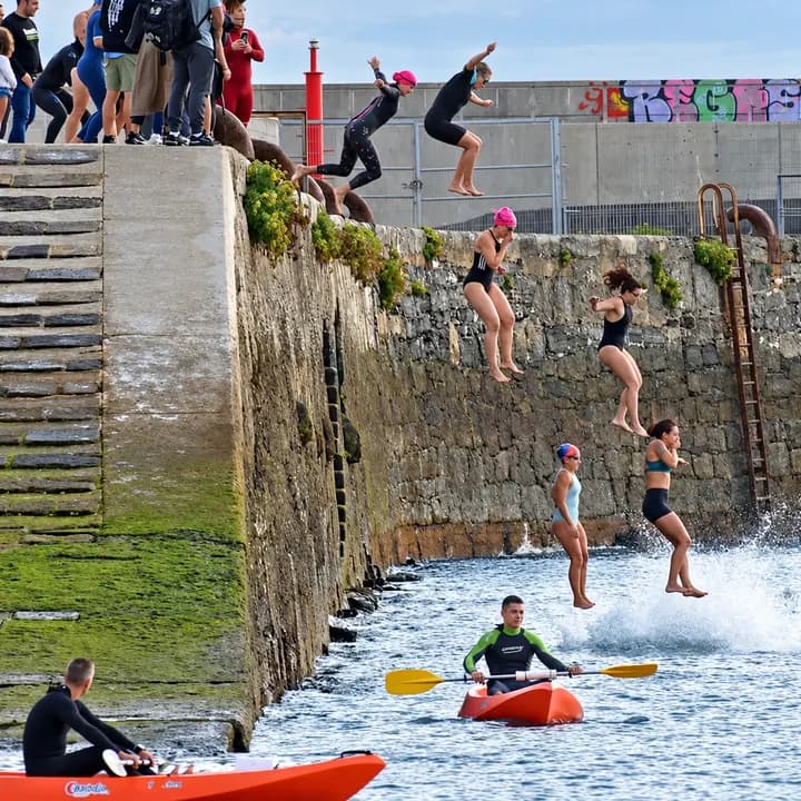 Participantes saltando al mar desde el muelle, junto a los kayaks
